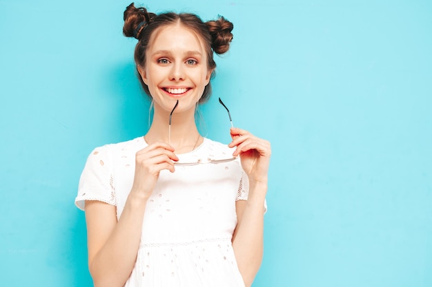 Photo gratuite jeune belle femme souriante en robe d'été à la mode sexy femme insouciante avec une coiffure à deux cornes posant près du mur bleu en studio modèle positif s'amusant