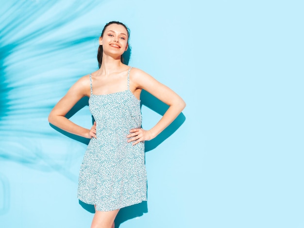 Jeune belle femme souriante en robe d'été à la mode Sexy femme insouciante posant près du mur bleu en studio Modèle brune positive s'amusantGai et heureux Isolé