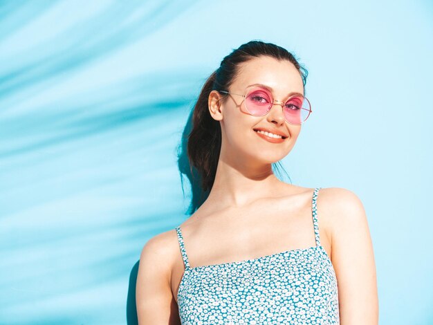 Jeune belle femme souriante en robe d'été à la mode Sexy femme insouciante posant près du mur bleu en studio Modèle brune positive s'amusantGai et heureux Isolé