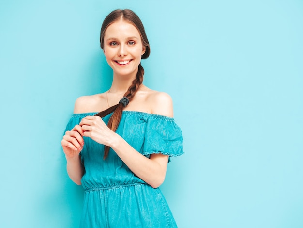 Jeune belle femme souriante en salopette de jeans d'été à la mode Femme insouciante sexy avec une coiffure de queue posant près du mur en studio Modèle positif s'amusant Gai et heureux Isolé