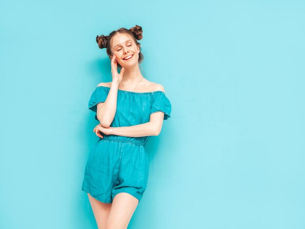 Jeune belle femme souriante en salopette de jeans d'été à la mode Sexy femme insouciante avec une coiffure à deux cornes posant près du mur en studio Modèle positif s'amusant Enthousiaste et heureux Isolé