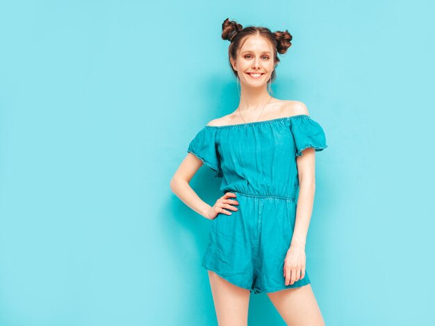 Jeune belle femme souriante en salopette de jeans d'été à la mode Sexy femme insouciante avec une coiffure à deux cornes posant près du mur en studio Modèle positif s'amusant Enthousiaste et heureux Isolé