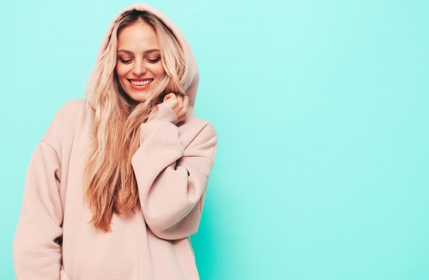 Jeune belle femme souriante en sweat à capuche d'été à la mode Sexy femme insouciante posant près du mur bleu en studio Modèle blond positif s'amusant et devenant fou Gai et heureux Dans le capot