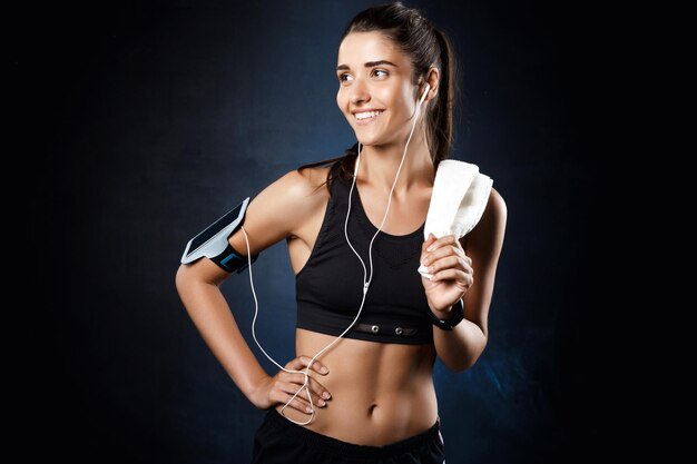 Jeune belle femme sportive brune écoutant de la musique sur un mur sombre