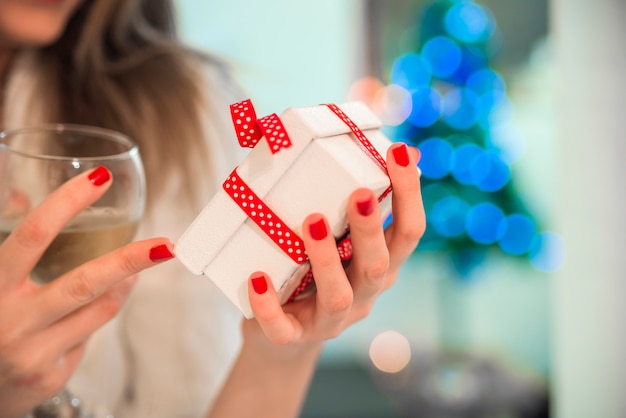 Jeune belle femme tenant Chrismtas présente dans ses mains devant un arbre de Noël magnifiquement décoré.