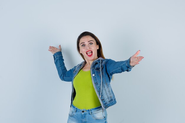 Jeune belle femme en tenue de denim ouvrant les bras pour un câlin et ayant l'air heureuse, vue de face.