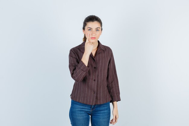 Jeune belle femme tirant la paupière vers le bas en veste et l'air pensif. vue de face.