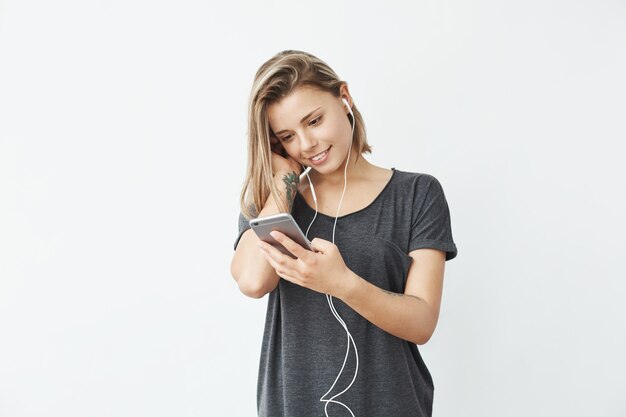 Jeune belle fille au casque souriant en regardant l'écran du téléphone.