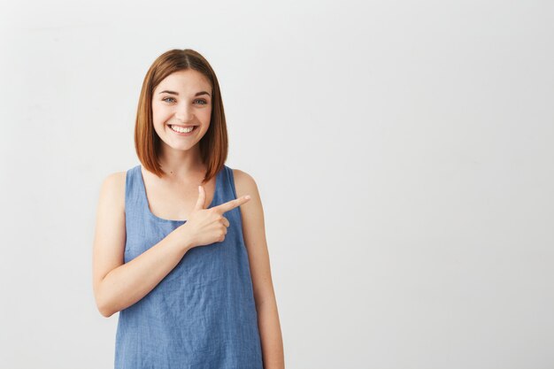 Jeune belle fille brune souriante pointant le doigt sur le côté.