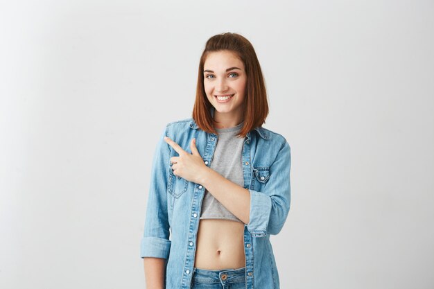 Jeune belle fille brune souriante pointant le doigt sur le côté.