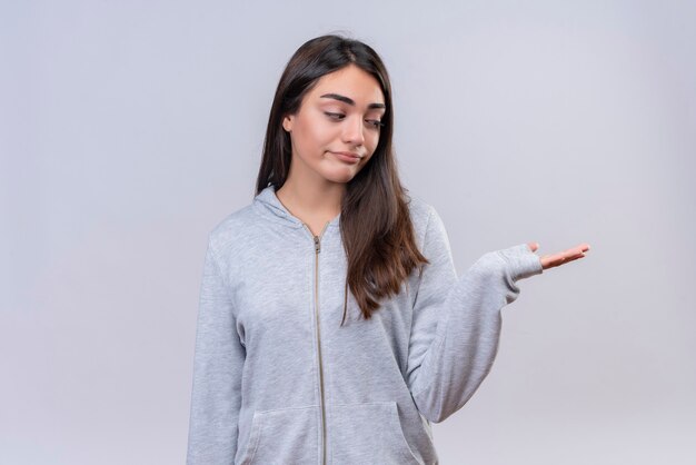 Jeune belle fille à capuche gris à la main avec le visage ennuyé debout sur fond blanc