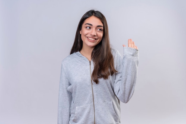 Jeune belle fille à capuche gris à la recherche de suite faisant salut geste debout sur fond blanc