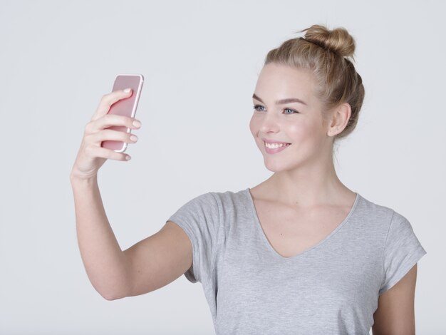 Jeune belle fille caucasienne fait des selfies. Heureuse femme merveilleuse avec un téléphone portable en mains