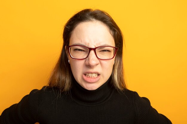 Jeune belle fille dans un col roulé noir et des lunettes mécontent de visage en colère