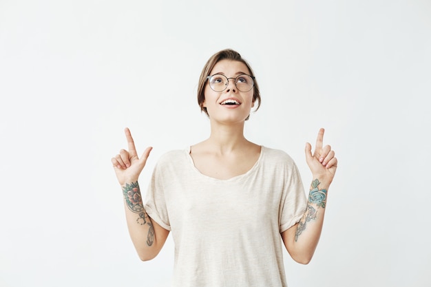 Jeune belle fille dans des verres souriant pointant les doigts vers le haut.