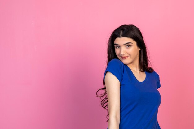 Jeune belle fille debout sur fond rose et portant un t-shirt bleu Photo de haute qualité