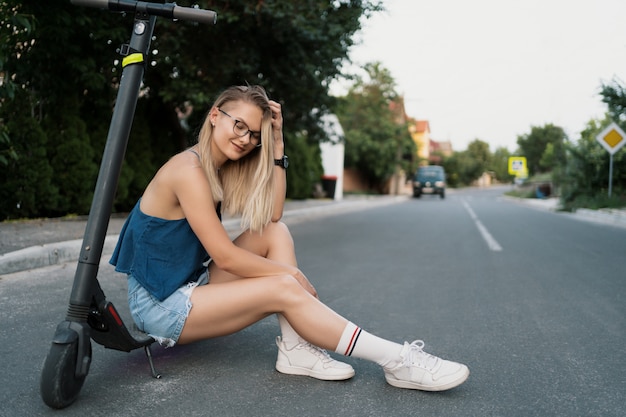 Jeune belle fille est assise sur son scooter électrique en été dans la rue