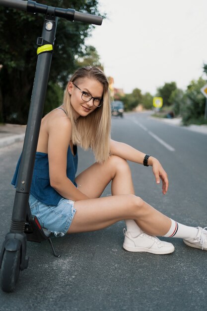 Jeune belle fille est assise sur son scooter électrique en été dans la rue