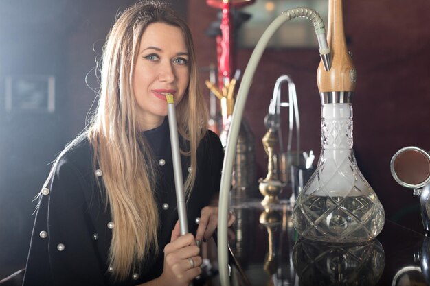 La jeune belle fille fume un narguilé