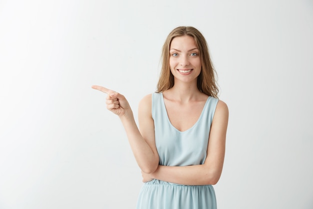 Photo gratuite jeune belle fille joyeuse souriant doigt pointé sur le côté sur fond blanc.