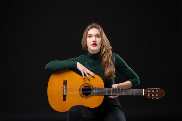 Jeune belle fille de musicien fatigué tenant la guitare sur l'obscurité