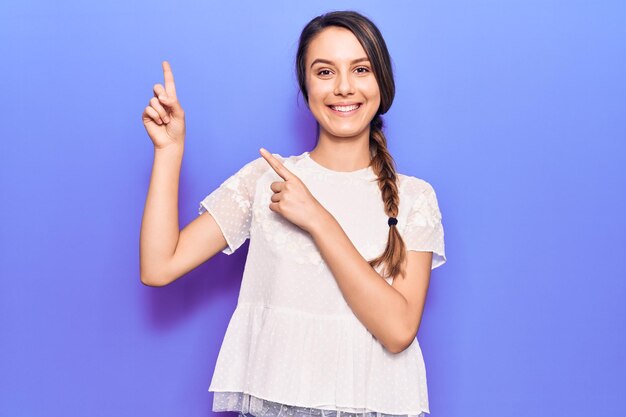 Jeune belle fille portant un t-shirt décontracté souriant et regardant la caméra pointant avec deux mains et doigts sur le côté.