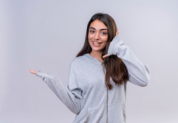 Jeune belle fille regardant la caméra joyeusement et faisant appelez-moi le geste debout sur fond blanc