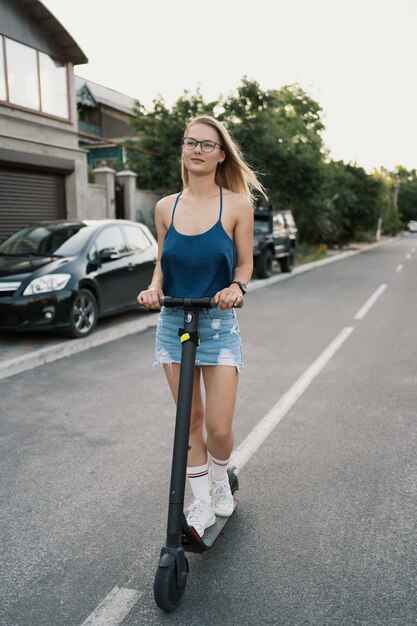 Jeune belle fille sur un scooter électrique en été dans la rue