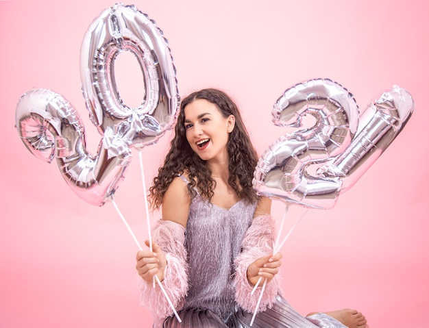 Jeune belle fille se réjouit de la nouvelle année sur un fond rose avec des ballons d'argent pour le concept de nouvel an