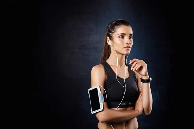 Jeune belle fille sportive écoute de la musique sur un mur sombre.