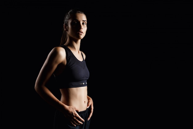 Jeune belle fille sportive posant sur un mur sombre.