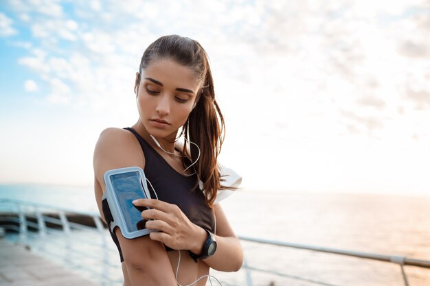 Jeune belle fille sportive s'entraînant au lever du soleil sur le bord de mer.