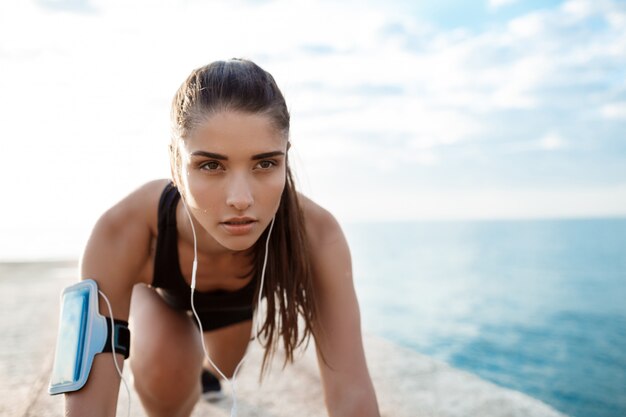 Jeune belle fille sportive se prépare à courir au bord de mer.