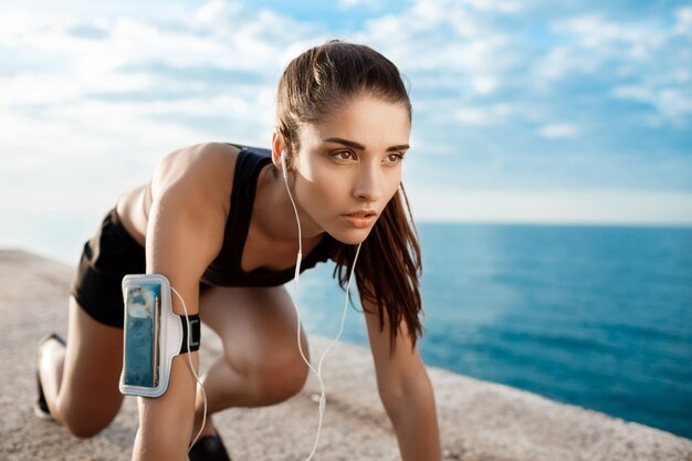 Jeune belle fille sportive se prépare à courir au bord de mer.