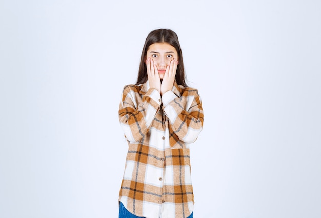 jeune belle fille en tenue décontractée tenant son visage sur un mur blanc.