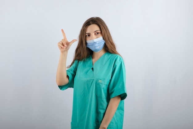 Jeune belle infirmière en uniforme vert dans un masque médical pointant vers le haut