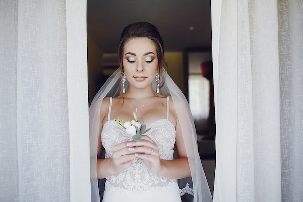 Photo gratuite une jeune et belle mariée à la maison debout près de la fenêtre avec des fleurs