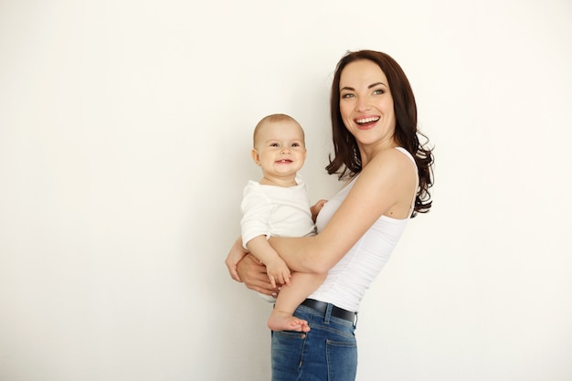 Jeune belle mère heureuse souriant rire tenant sa petite fille sur le mur blanc.