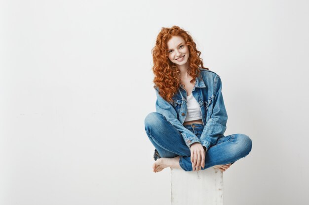 Jeune belle rousse souriante assise sur une boîte. Copiez l'espace.