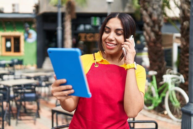 Photo gratuite jeune belle serveuse arabe parlant sur un smartphone à l'aide du pavé tactile sur la terrasse du café