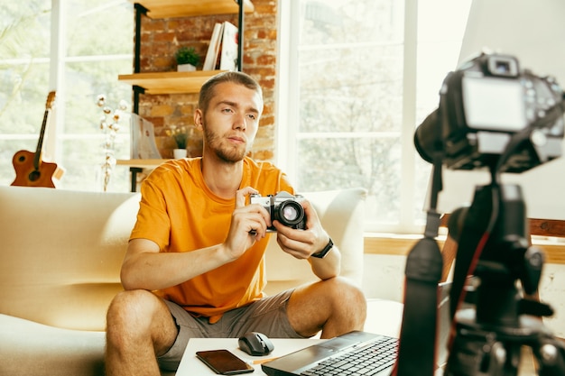 Jeune Blogueur Caucasien Avec équipement Professionnel Enregistrement Vidéo Examen De La Caméra à La Maison. Blog, Vidéoblog, Vlog. Homme Faisant Un Vlog Ou Un Flux En Direct Sur La Photo Ou La Nouveauté Technique.