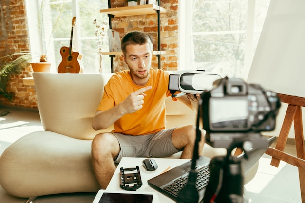 Photo gratuite jeune blogueur caucasien avec équipement professionnel enregistrement vidéo examen de lunettes vr à la maison. blog, vidéoblog, vlog. l'homme évalue le casque de réalité virtuelle lors de la diffusion en direct.