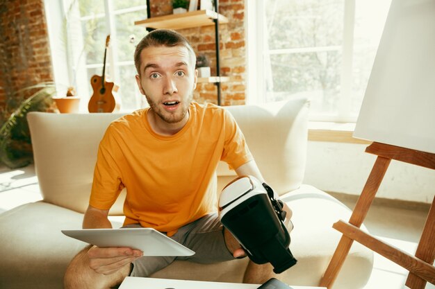 Jeune blogueur caucasien avec équipement professionnel enregistrement vidéo examen de lunettes VR à la maison. Blog, vidéoblog, vlog. Homme faisant un vlog ou un flux en direct sur la photo ou la nouveauté technique.