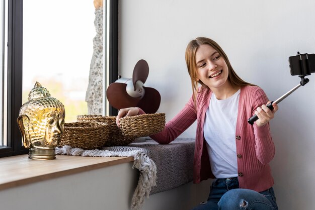 Jeune blogueuse s'enregistre à côté d'une fenêtre montrant la décoration intérieure