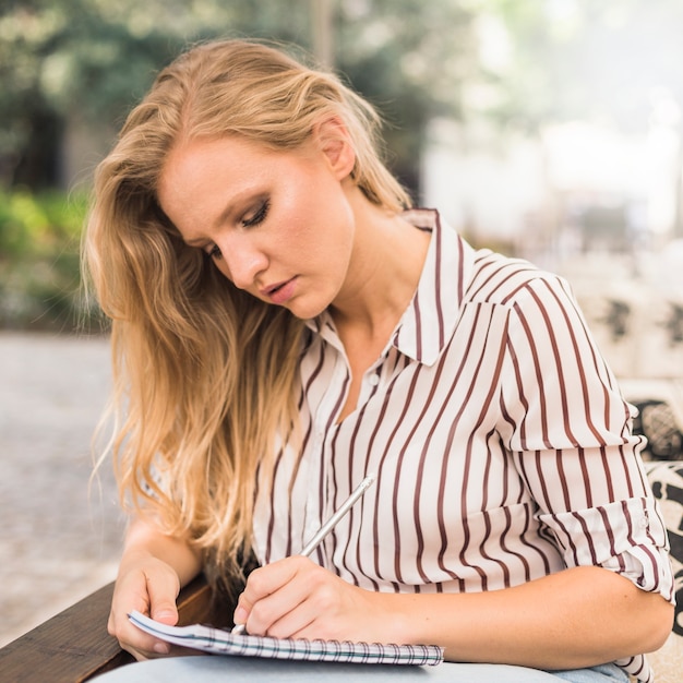 Jeune blonde écrit sur un cahier avec un crayon