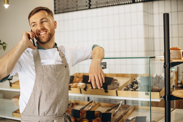 Jeune boulanger debout près du comptoir et parler au téléphone