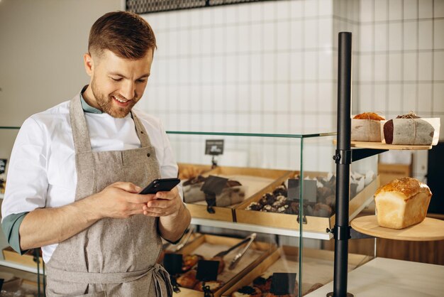 Jeune boulanger debout près du comptoir et parler au téléphone