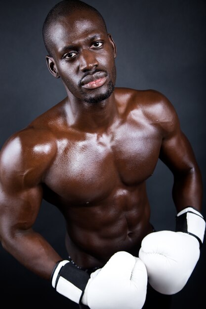 Jeune boxeur athlétique portant des gants en fond noir.