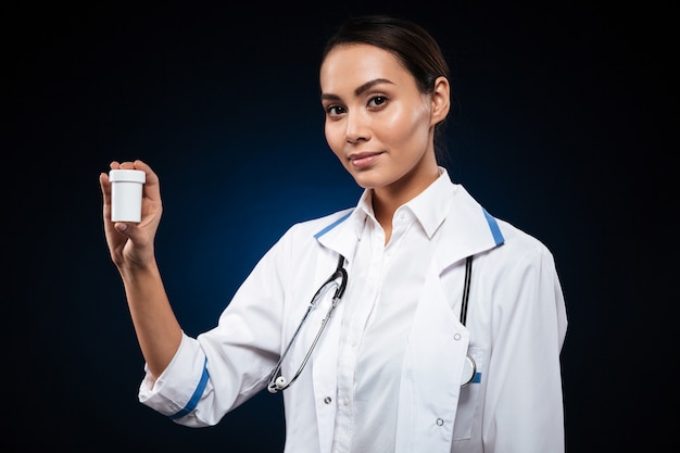 Jeune brune infirmière montrant une bouteille avec des pilules isolées