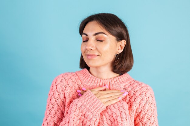 Jeune brune en pull rose chaud isolé sur mur bleu